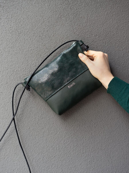 Handtasche in dunkelgrün mit Prägung in Schlangenoptik vor grauer Wand